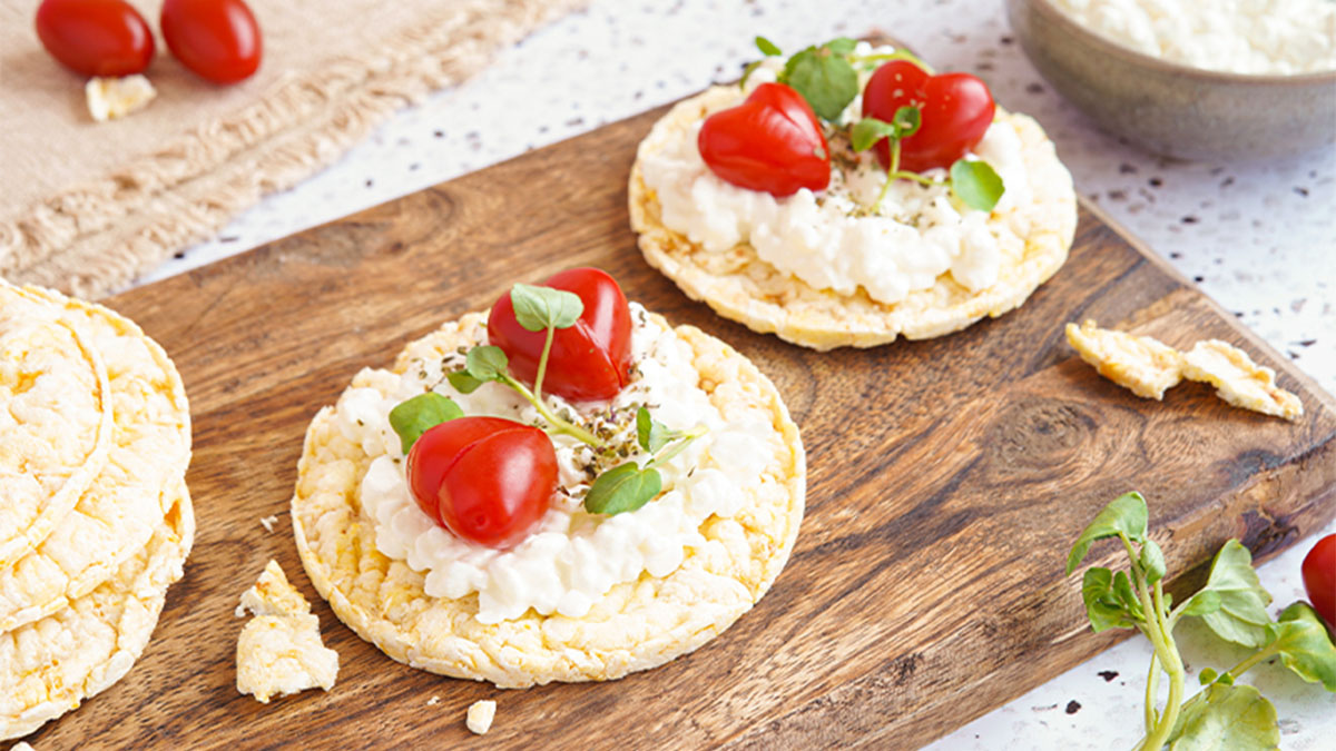 Tábua de madeira com bolachas de arroz ou milho, com queijo e tomate cherry